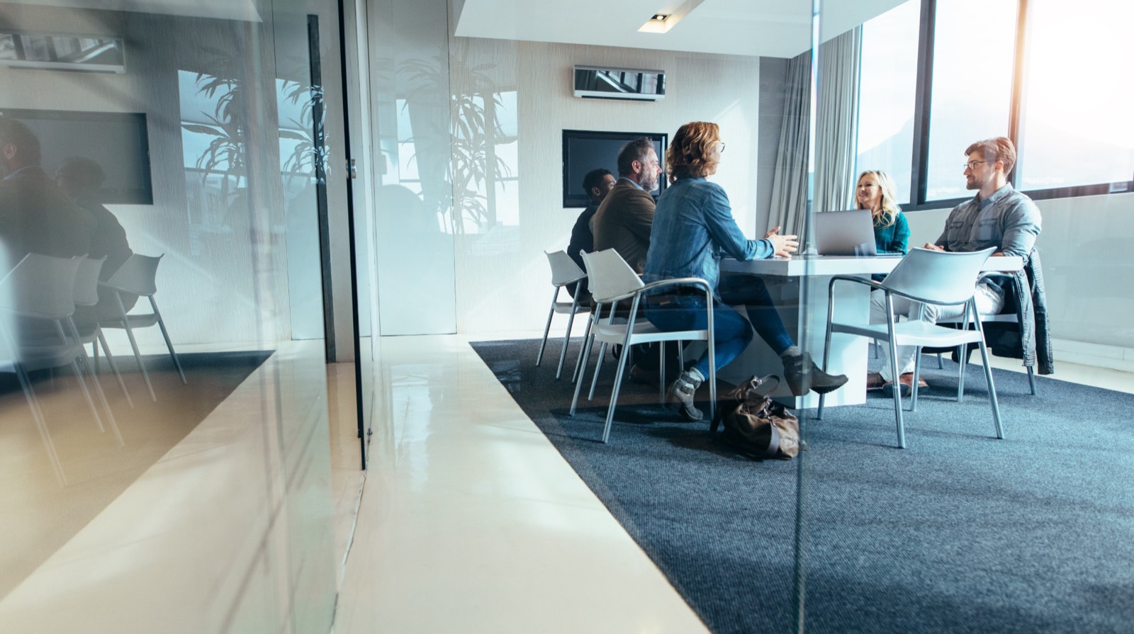 Five people meeting around a table in a glass-walled room